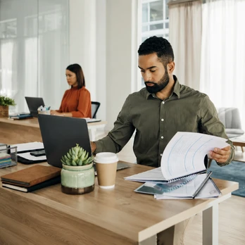 Office professional reviewing documents on laptop and papers, representing business process automation with Odoo customization services, replacing manual approvals and spreadsheet-based workflows for better efficiency.