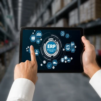 Hands interacting with a tablet displaying ERP dashboard icons inside a warehouse environment, representing Odoo customization services for industry-specific workflows in manufacturing, retail, real estate, and hospitality ERP systems.